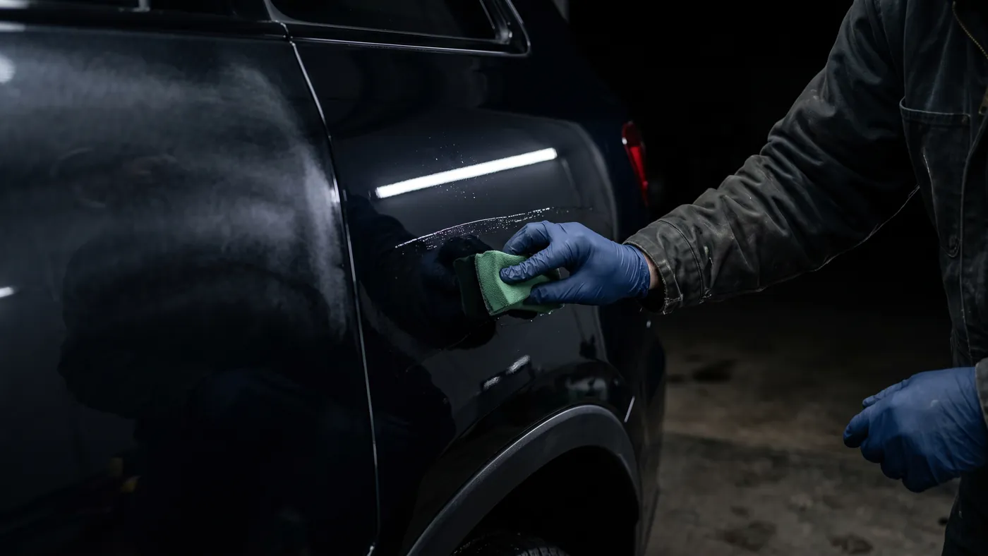 A technician working a microfibre applicator pad along the rear quarter of a dark SUV