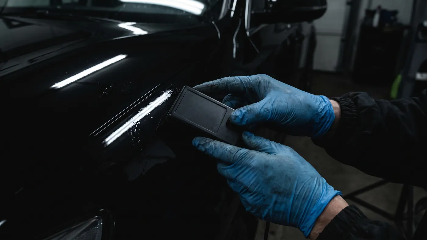 A certified technician checking coated paint with a handheld thickness gauge in a dark bay