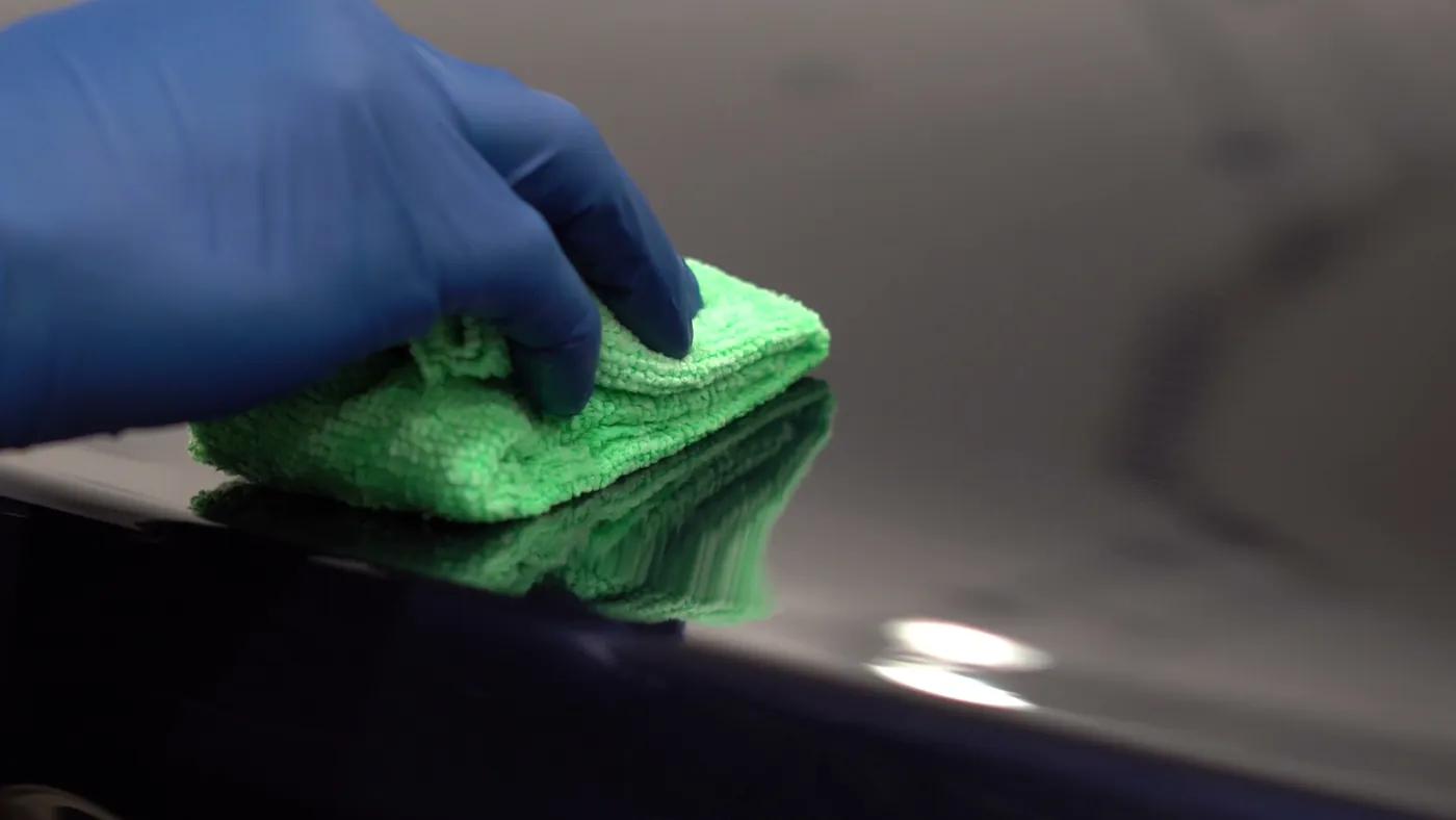 A gloved technician pressing a microfibre applicator onto a black glossy fender
