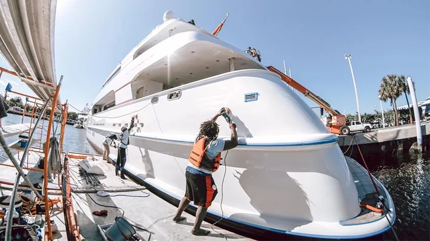 Crew detailing the hull of a large yacht in a marina