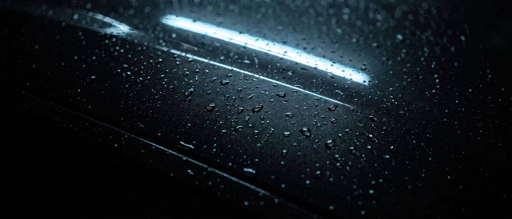 Rain beaded across black coated paint under one cool light bar
