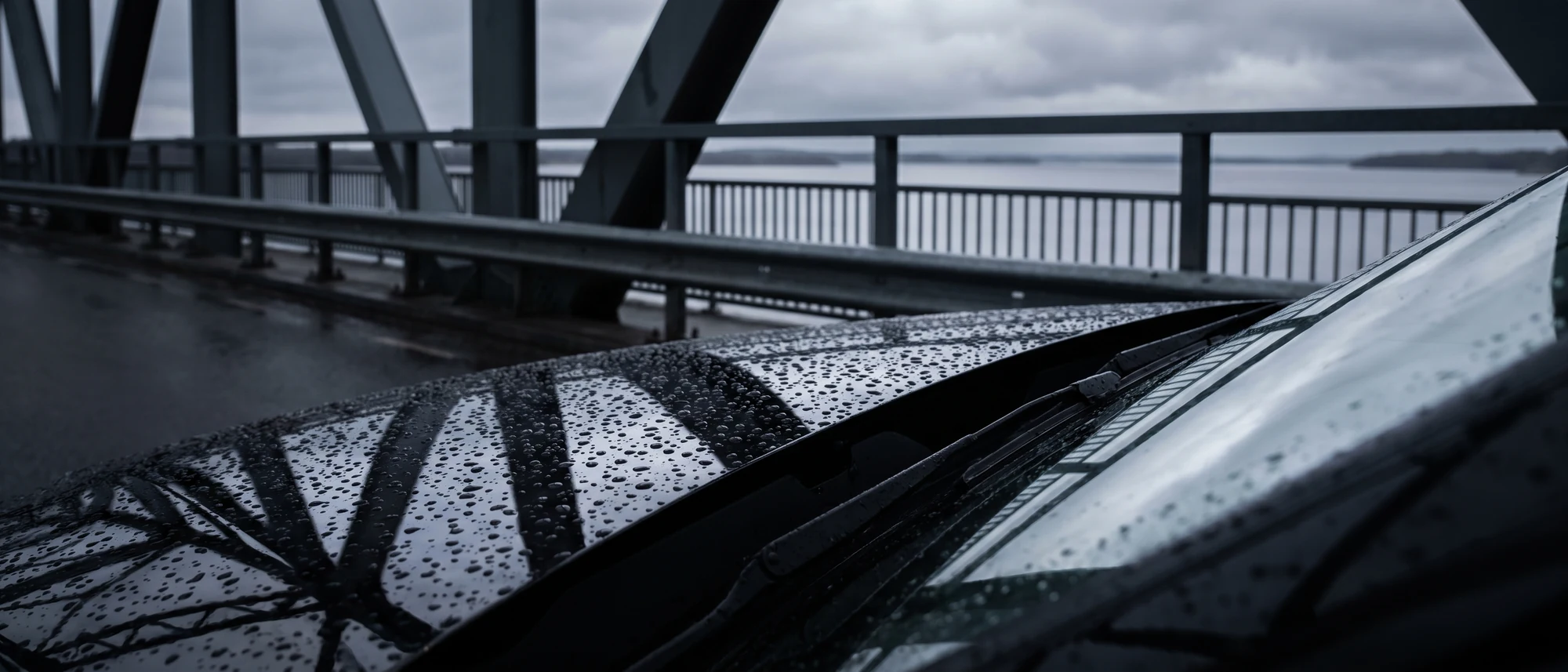 Water beaded on a coated black bonnet with a high bridge deck out of focus behind it