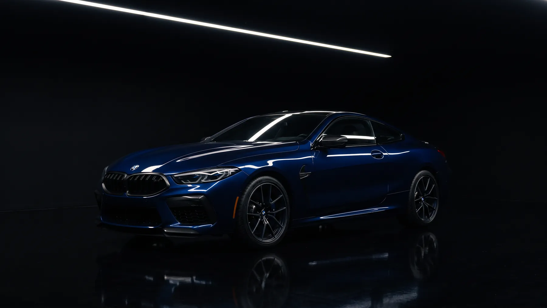A midnight blue coupe finished with ICON Rocklear, front three quarter under a single strip light in a dark studio