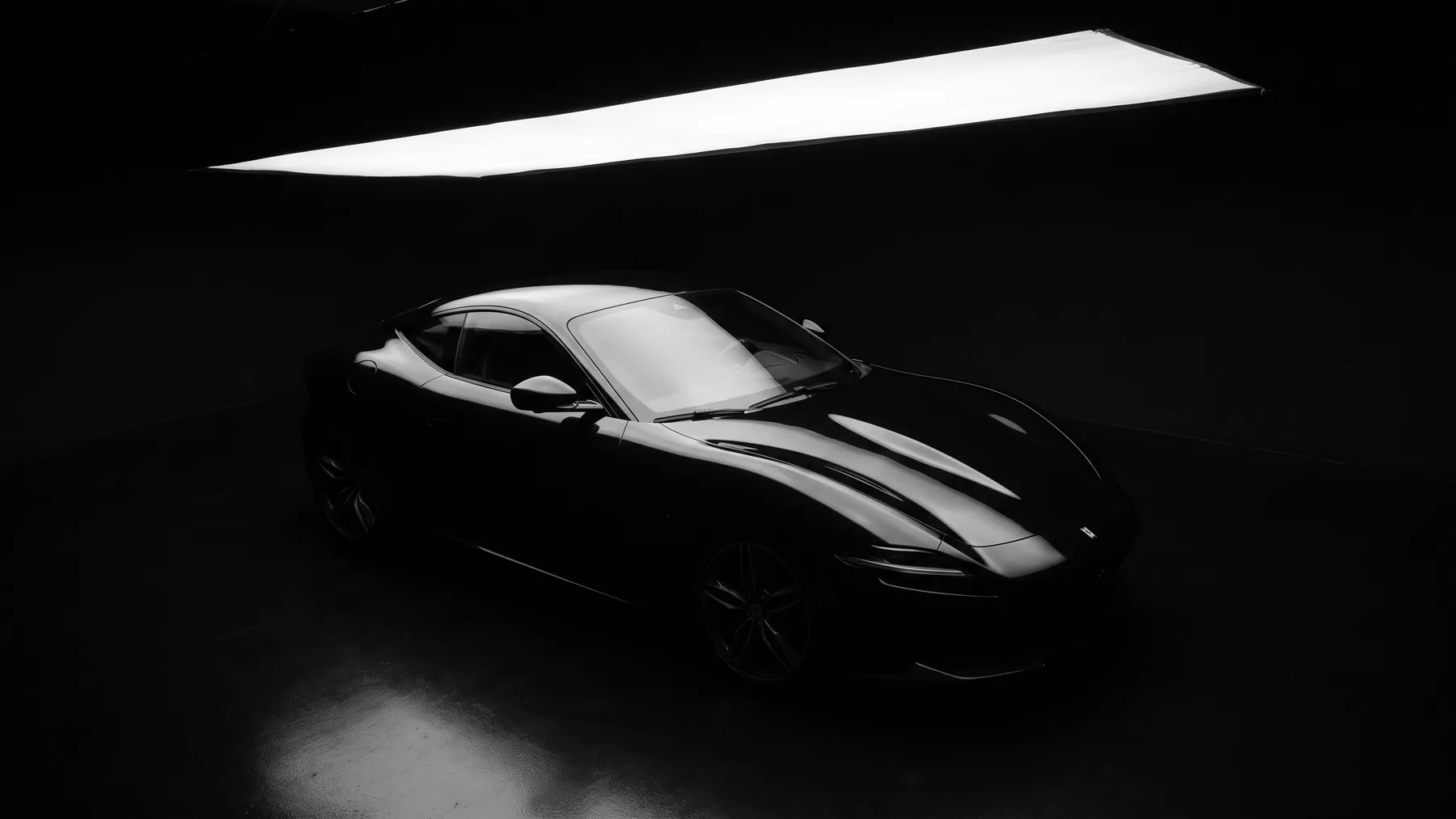 A black coupe seen from a high three quarter, one long light running the length of the car