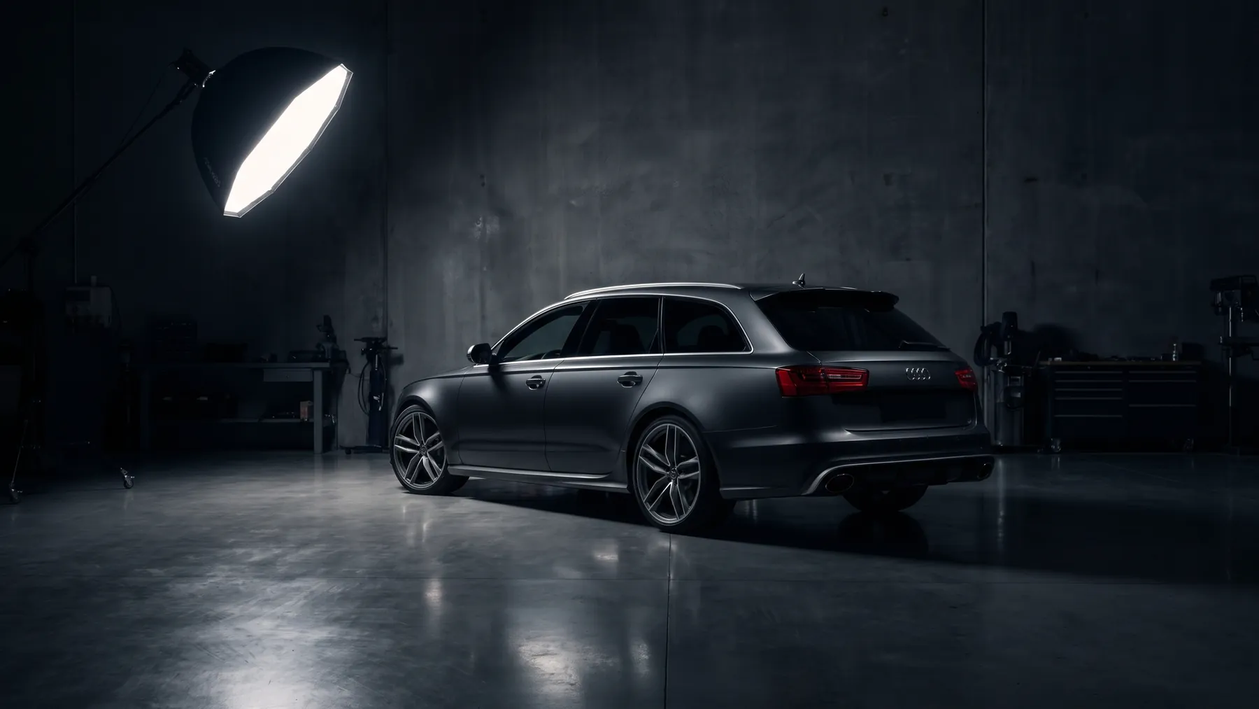 A dark graphite estate car, rear three quarter, lit by a single softbox in a workshop studio