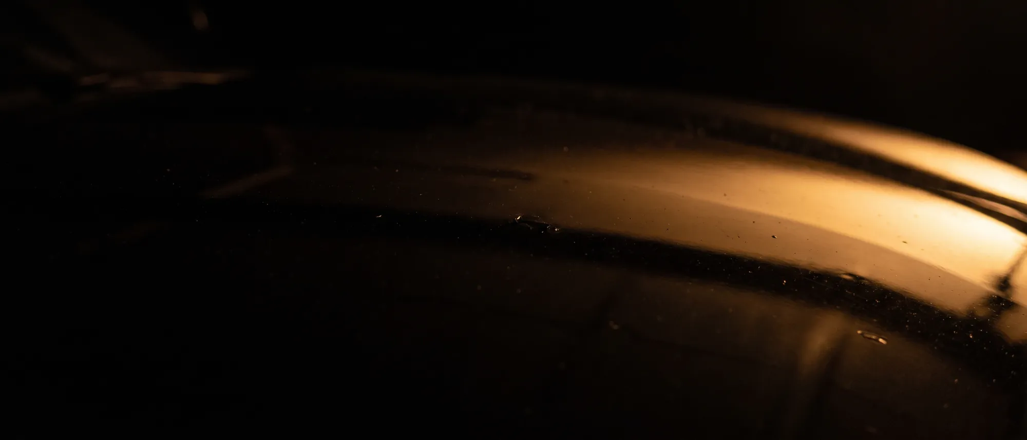 Warm light falling away across the gloss shoulder of a black coated panel