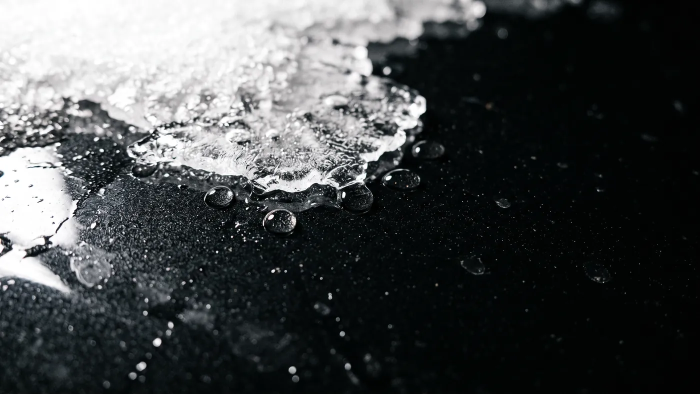 Melting snow and thin ice pulling into water beads on gloss black coated paint