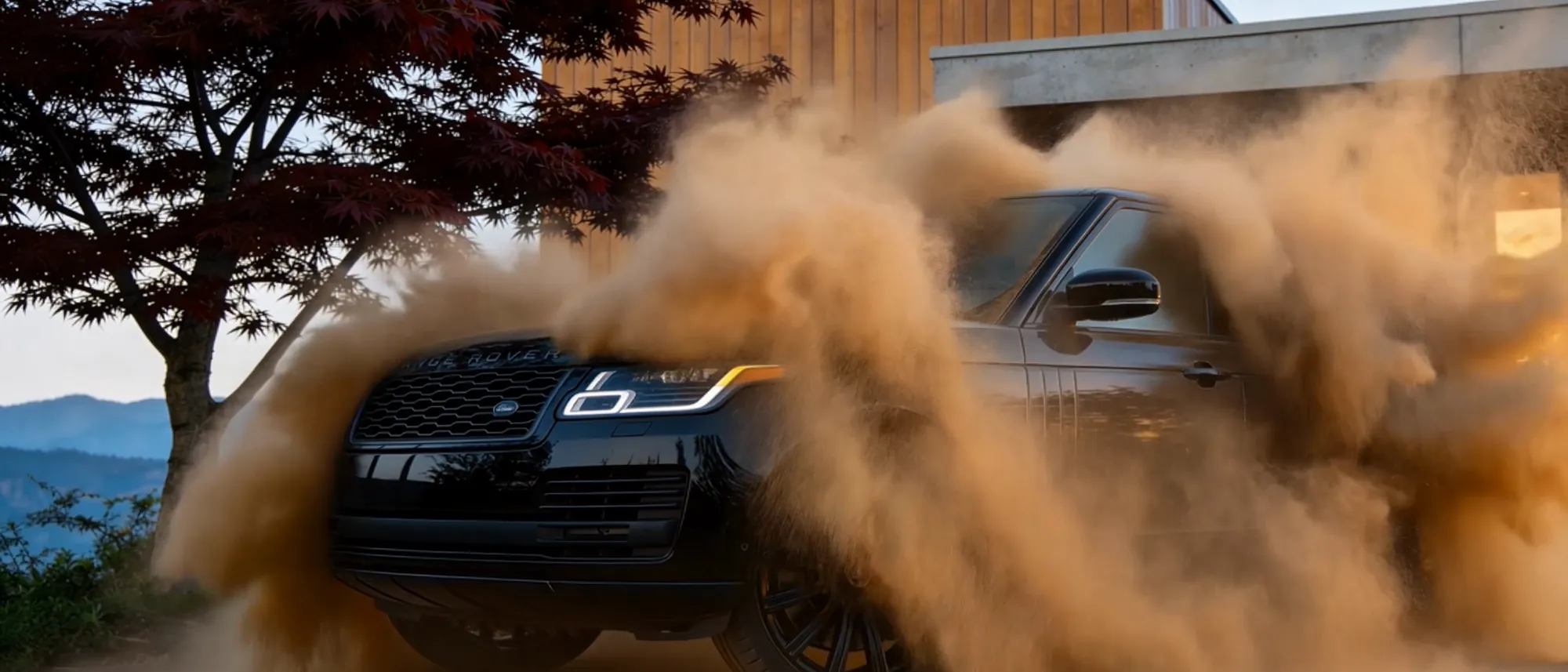 A black Range Rover throwing up dust at dusk, its coated paint still holding the light