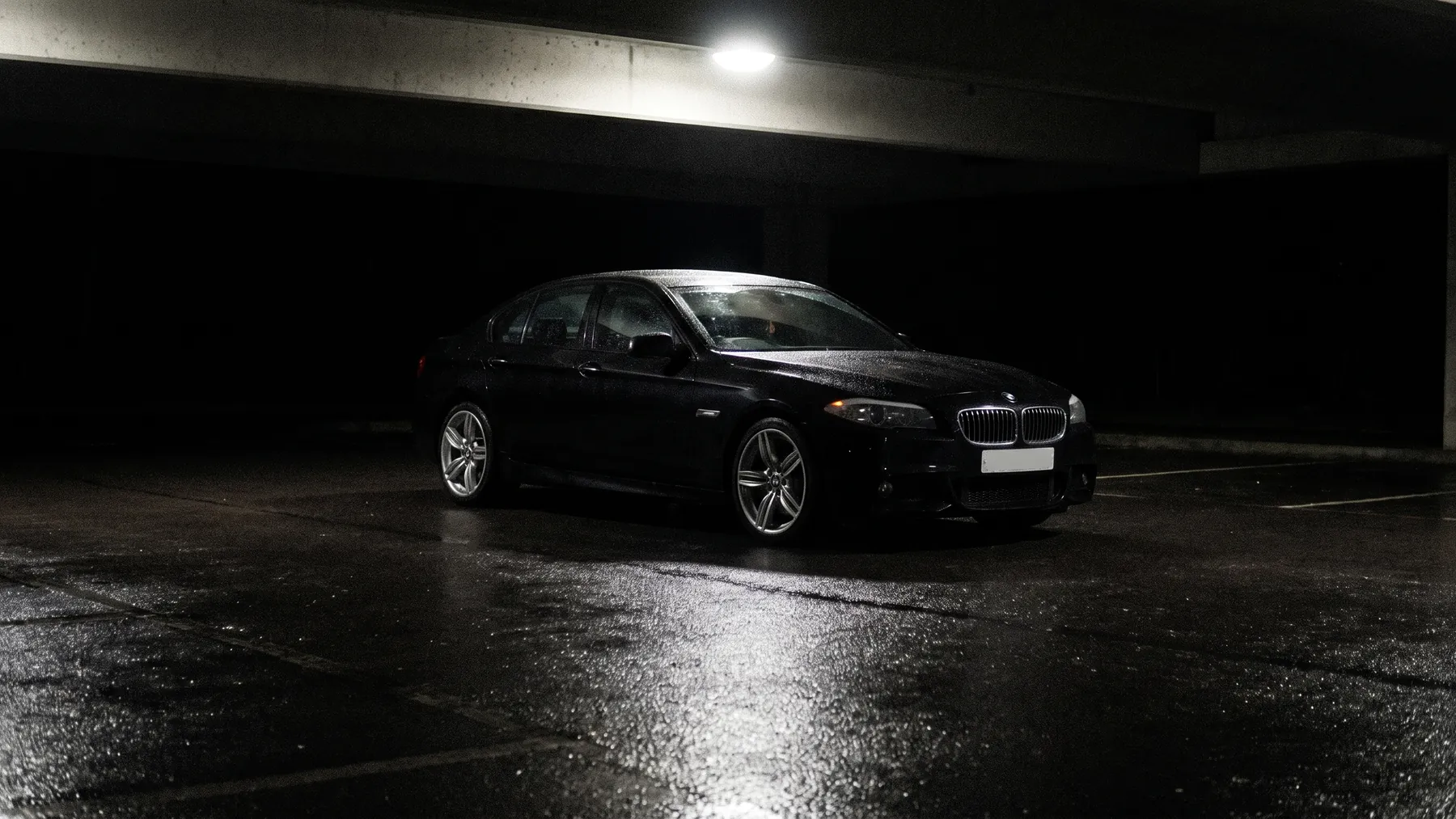 A black saloon on wet dark asphalt under cover, reflected in the ground beneath it