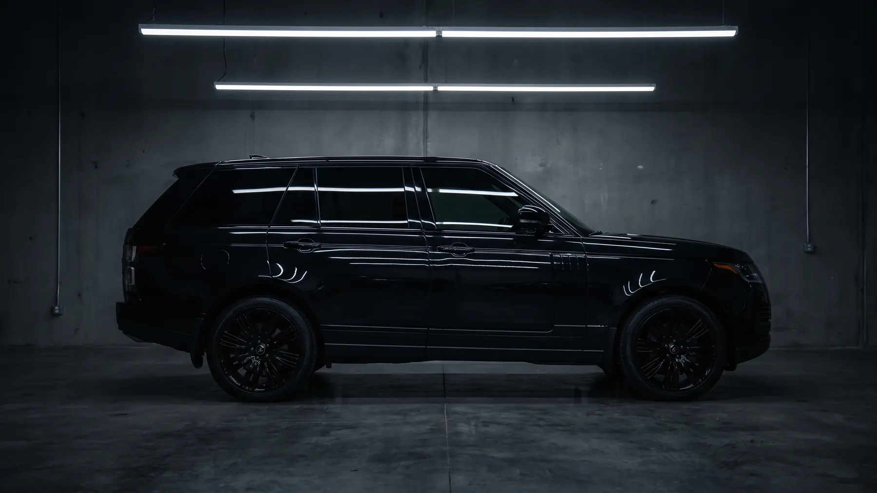 A gloss black full size SUV in exact side profile inside a dark certified bay