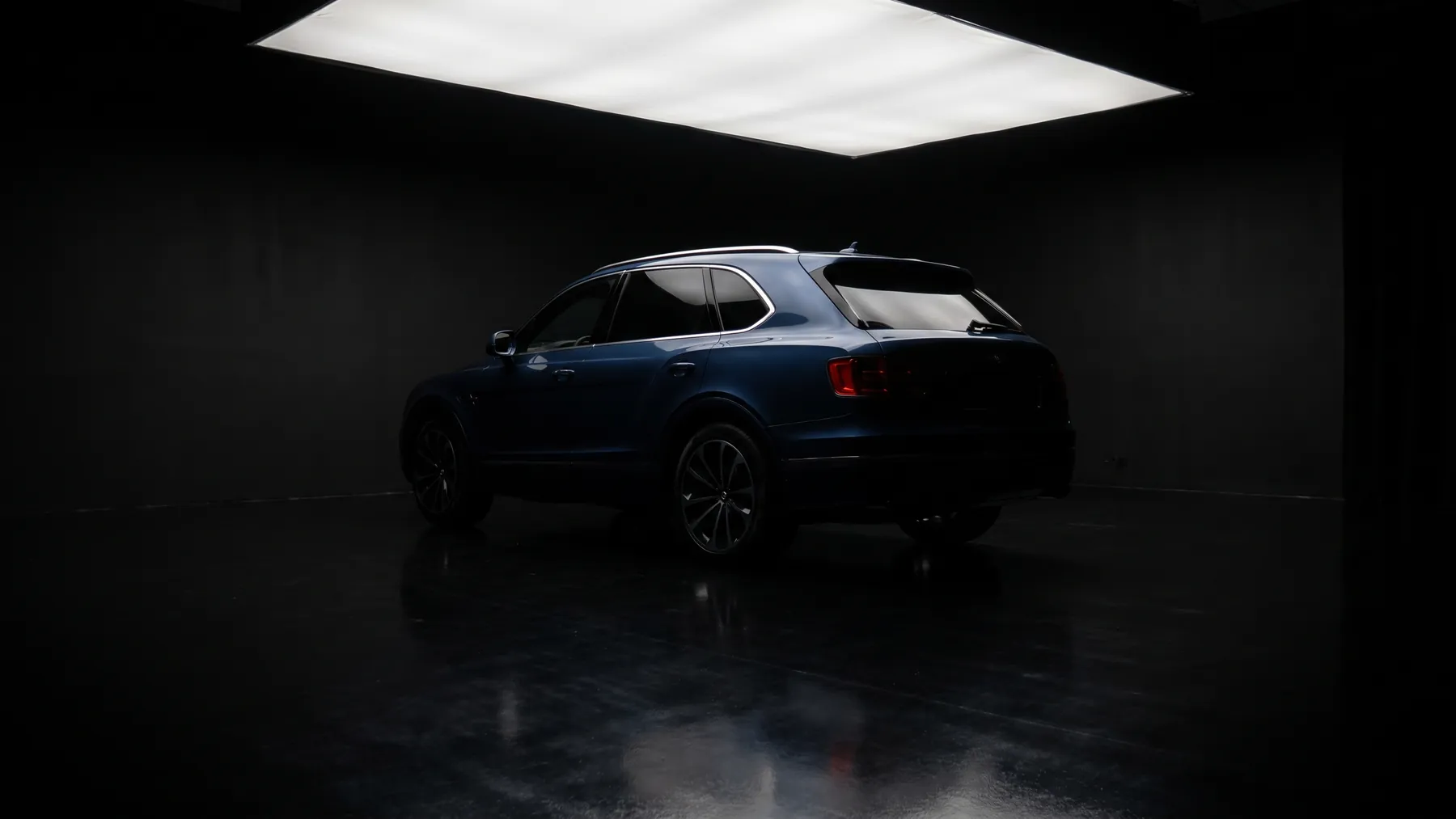 A dark blue SUV, rear three quarter, under a softbox with deep shadow around it